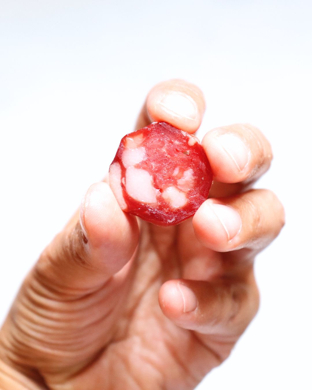 Salame ahumado en mano, mostrando su textura artesanal y color vibrante, ideal para degustar.